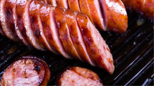 Sliced grilled sausage with a glossy glaze, resting on a dark grill surface.