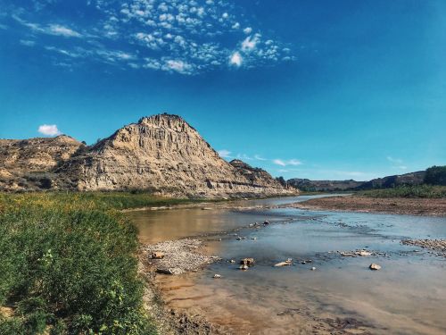 A serene landscape featuring a river winding through rocky terrain under a clear blue sky.