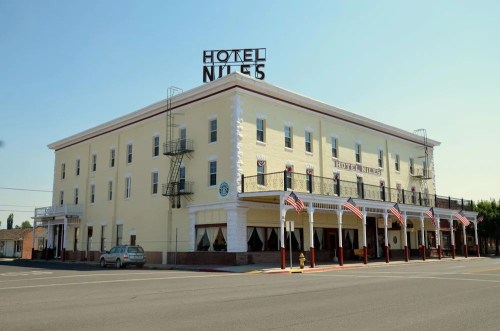 Historic yellow hotel building with a sign reading "Hotel Niles," featuring American flags and a clear blue sky.