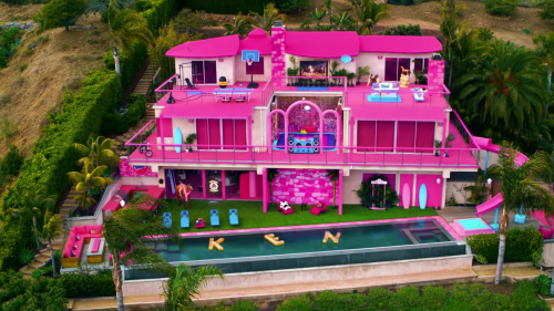 A vibrant pink mansion with a pool, palm trees, and playful decorations, featuring the name "KEN" in large letters on the lawn.