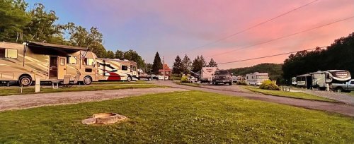 A scenic RV park at sunset, featuring several parked RVs and lush green grass under a colorful sky.