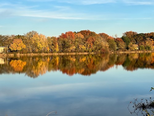 A serene lake reflecting vibrant autumn foliage and a clear blue sky.