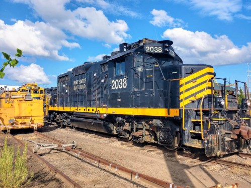A black and yellow locomotive labeled "2038" parked on railway tracks under a blue sky with clouds.
