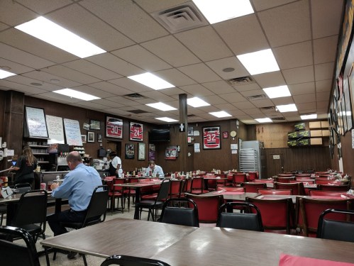 A cozy diner interior with red tables and chairs, featuring a few patrons and sports memorabilia on the walls.