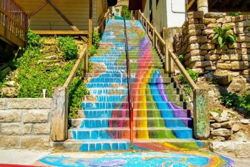 Colorful rainbow mural on stairs, blending vibrant hues with a natural stone backdrop and greenery.