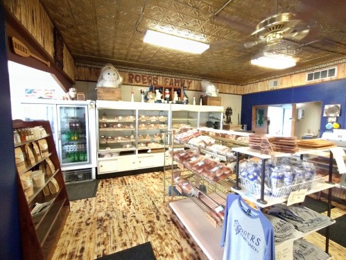 A cozy bakery interior with display cases of baked goods, a fridge, and rustic decor featuring a ceiling fan.