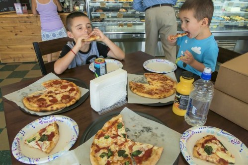 Two children enjoy pizza at a table with multiple pizza slices and drinks in a casual dining setting.