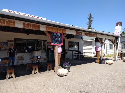 A small eatery with outdoor seating, featuring a menu board and a sign displaying hours of operation.