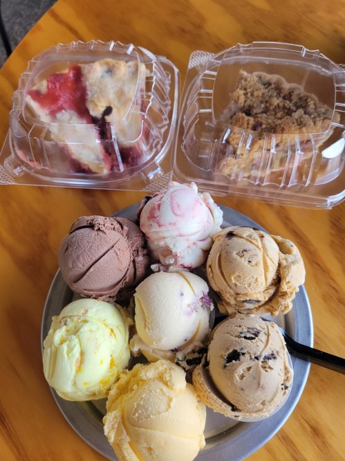 A plate of assorted ice cream scoops in various flavors, with two containers of dessert in the background.