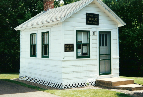 A small, white historic library building with green trim and a sign reading "Library" and "Closed" on the door.
