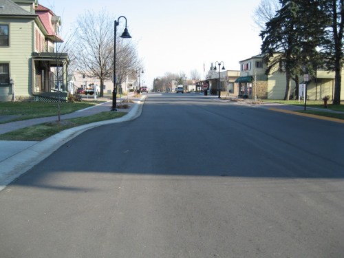 A quiet street lined with houses and shops, featuring lampposts and bare trees under a clear sky.