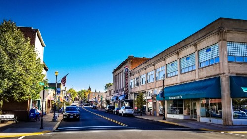 A sunny street view of a small town with shops, trees, and a clear blue sky.