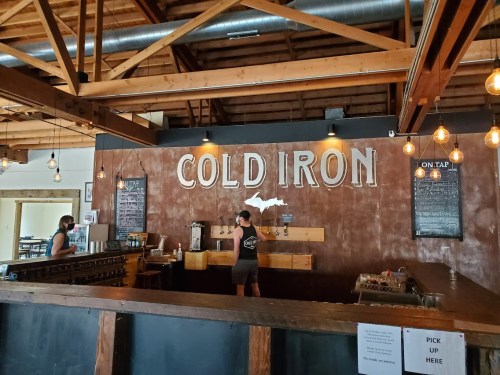 A barista serves customers at Cold Iron, a cozy brewery with wooden beams and a chalkboard menu.