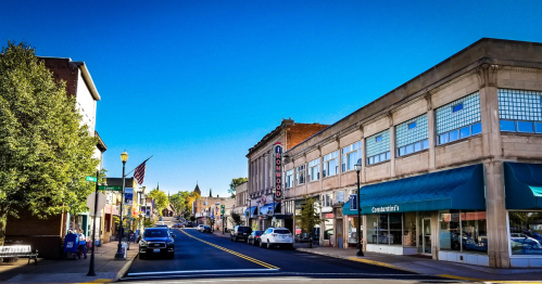 A sunny street view of a small town with shops, trees, and a clear blue sky.