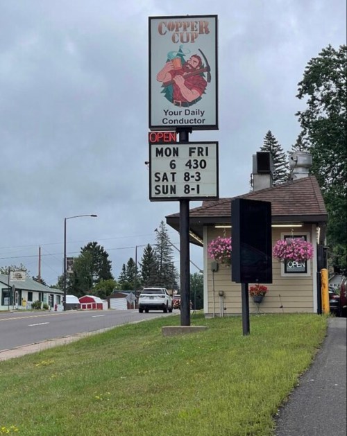Sign for Copper Cup with hours: Mon-Fri 6:30, Sat 8-3, Sun 8-1. Flowers in planters, cloudy sky in background.
