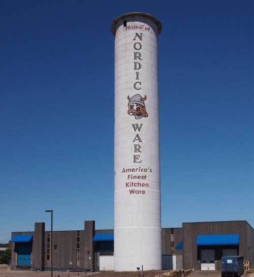 A tall water tower with "Home of Nordic Ware" and a Viking logo, set against a clear blue sky.