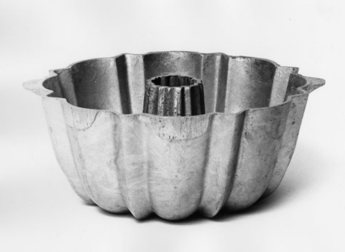 A vintage metal bundt cake pan with a fluted design and a central tube, set against a plain background.