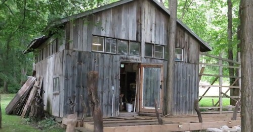 A rustic wooden cabin surrounded by trees, featuring large windows and a porch.