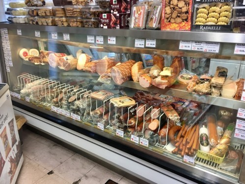 A display case filled with various meats, including hams, sausages, and cured products, in a deli setting.