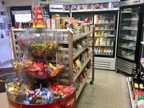 A convenience store interior featuring shelves of snacks, a candy display, and a refrigerated section.