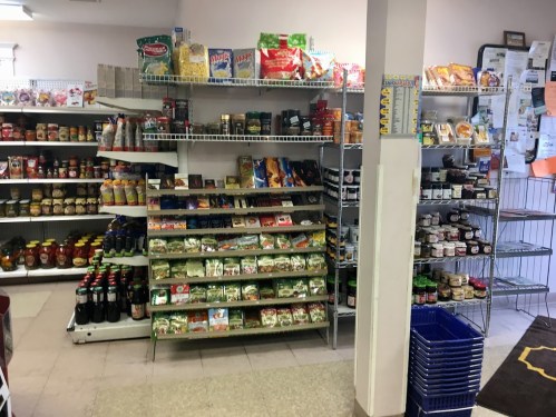 A small grocery store interior with shelves stocked with various food items, snacks, and beverages.