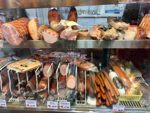 A display case filled with various types of meats, including sausages, cured meats, and cheeses, with price tags visible.
