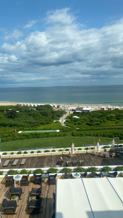 A scenic view of a beach with green landscaping, wooden deck, and cloudy sky in the background.