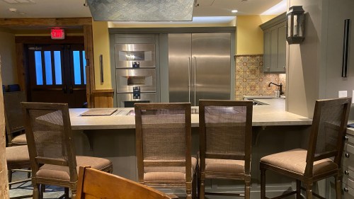 Modern kitchen with stainless steel appliances, a large island, and bar stools, featuring warm lighting and decorative tiles.