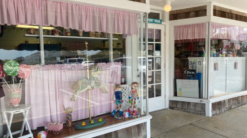 A charming storefront with pink curtains, featuring a carousel horse and colorful decorations in the window display.