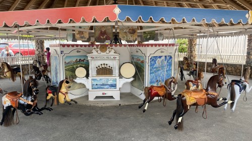 A vintage carousel with wooden horses, colorful canopies, and a decorative backdrop, set in a covered area.