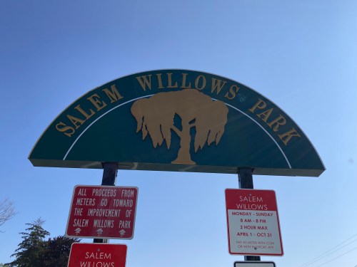Sign for Salem Willows Park with a tree graphic, displaying park hours and information about meter proceeds.