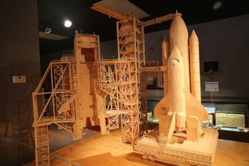 A detailed wooden model of a space shuttle and launch pad, showcasing intricate craftsmanship and design.