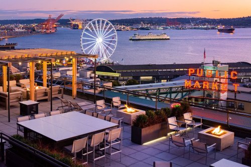 Rooftop view of Seattle's waterfront at sunset, featuring the Ferris wheel and iconic Public Market sign.