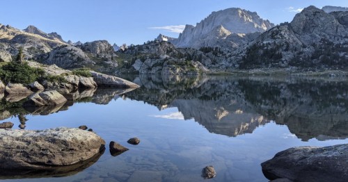 A serene mountain landscape reflecting in a calm lake, surrounded by rocky terrain and clear blue skies.