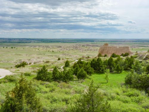 A vast landscape featuring green vegetation, rocky formations, and a cloudy sky in the distance.