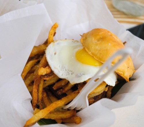 A burger topped with a fried egg, served with crispy fries in a paper-lined basket.