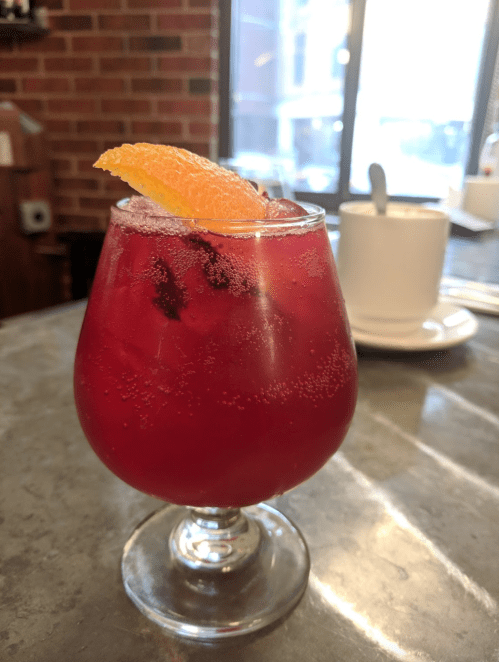 A refreshing red drink with bubbles, garnished with an orange slice, served in a round glass on a table.