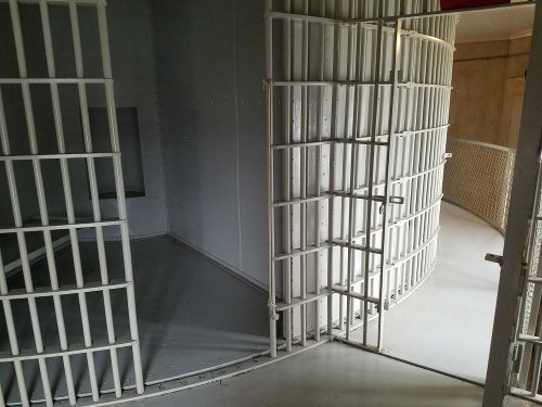 Interior view of a prison cell with barred doors, showcasing a circular layout and gray walls.