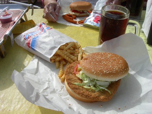 A sesame seed bun sandwich with lettuce, fries, and a drink on a yellow table.