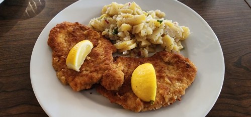 A plate featuring two breaded fried fish fillets with lemon slices, served alongside a portion of potato salad.