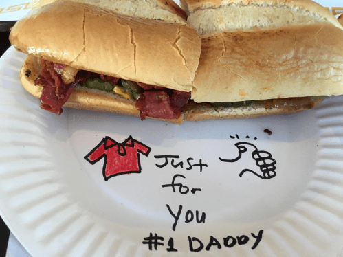 A sandwich on a paper plate with a drawing of a shirt and a thumbs-up, labeled "Just for You #1 DADDY."