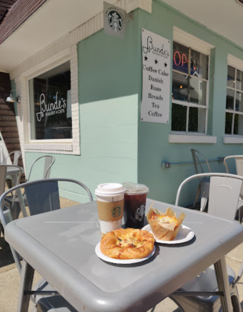 A table outside Bund's Bakery Cafe with coffee, iced drink, and a pastry in front of a light green building.