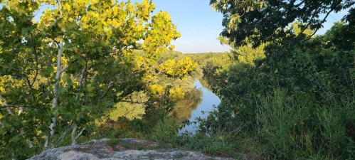 A serene river scene surrounded by lush green trees and bright yellow leaves under a clear blue sky.