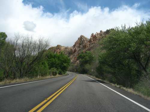 Winding road surrounded by lush greenery and rocky hills under a partly cloudy sky.