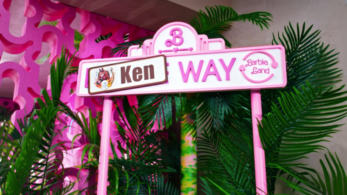 A pink street sign reading "Ken Way" in a vibrant, tropical setting with lush green plants.
