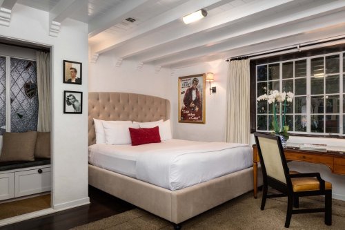 Cozy bedroom with a large bed, desk, and decorative artwork on the walls, featuring soft lighting and a warm atmosphere.