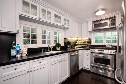 Modern kitchen with white cabinets, stainless steel appliances, and a black countertop, featuring a window and decorative plants.