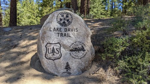 A large rock with engraved trail signs for Lake Davis Trail and U.S. Forest Service, surrounded by trees.