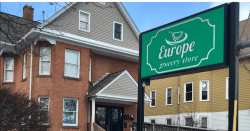 Sign for "Europe Grocery Store" in front of a two-story building with a mix of brick and siding.