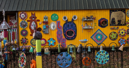 Colorful, whimsical art installation on a bright yellow wall, featuring various painted objects and decorations.